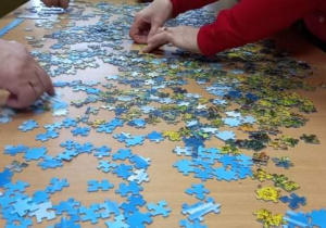 Seniorzy z Klubu "Senior+" układają puzzle.